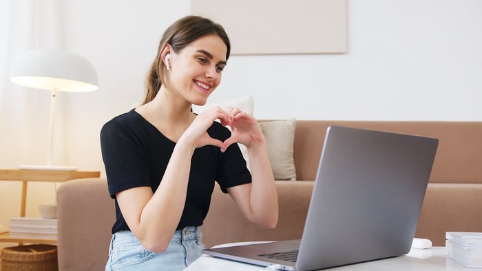 woman making heart shape towards laptop screen