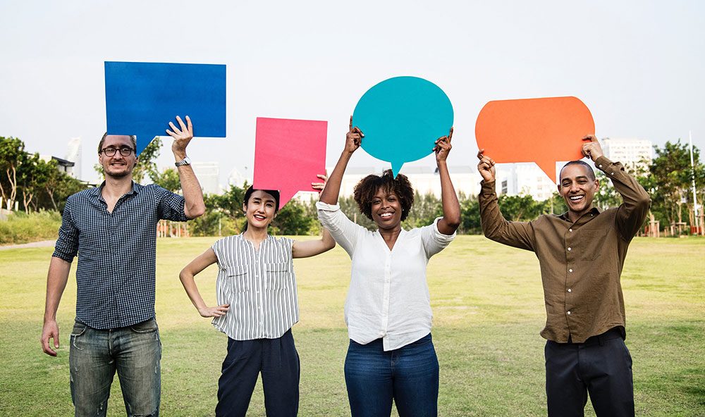 Four smiling young adults holding up coloured speech bubbles